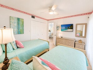 Ein Schlafzimmer mit zwei Betten, einem Deckenventilator, einem Gemälde, einer Kommode und einem Spiegel.