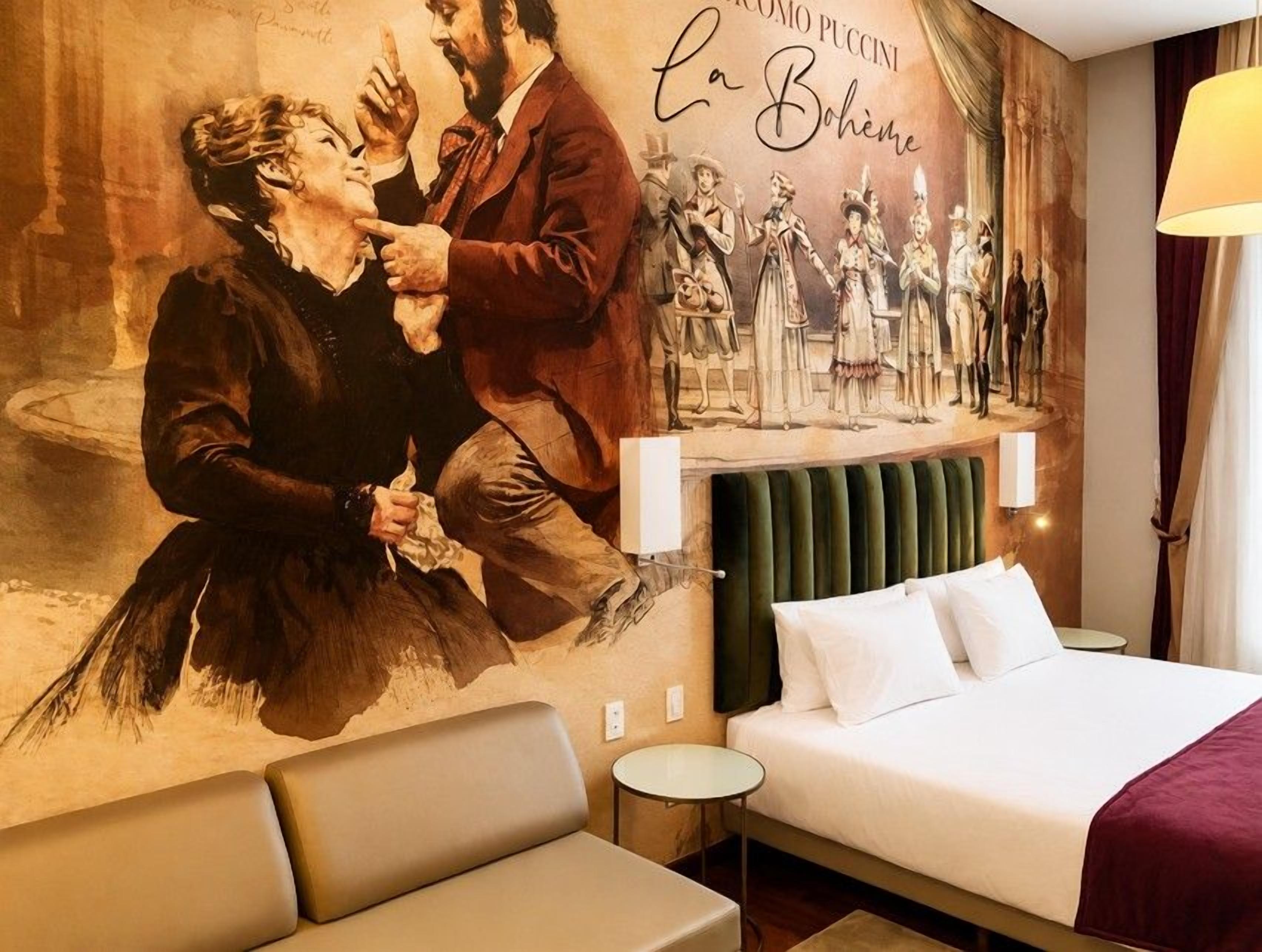 A hotel room with a large mural, a bed with white linens, a green headboard, and a small bedside table.