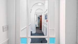 En hall med vita väggar, en blåmålad dörr och utsikt in i ett rum med ett element och ett träskåp.