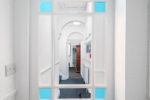 A hallway with white walls, a blue-framed door, and a view into a room with a radiator and a wooden cabinet. - Character filled 4 bed apartment in foody hotspot. (Redland)