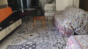 Een woonkamer met een bank, een televisie, een kleine tafel en een kitchenette.