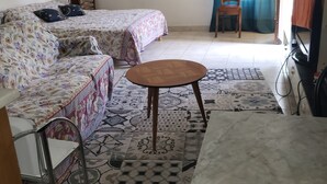 Een kamer met twee bedden, een tafel, een stoel, een ventilator en een televisie.