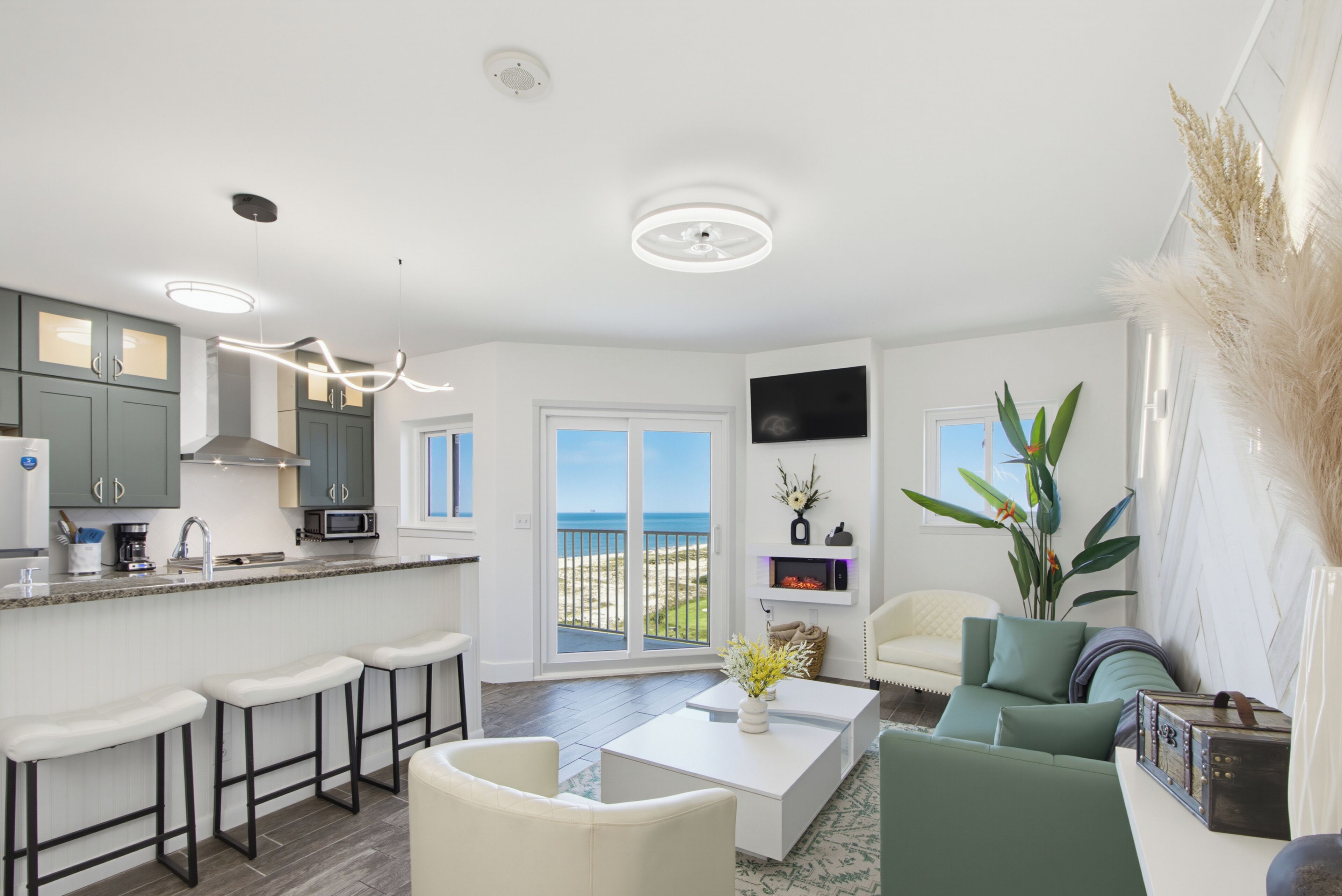 A modern kitchen with bar stools, a dining area with a white coffee table, and a view of the beach.