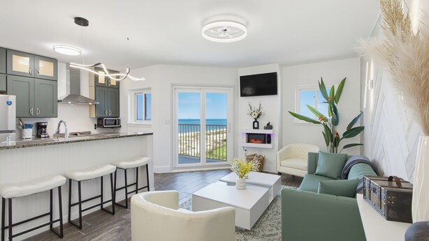 Une cuisine moderne avec des tabourets de bar, un coin repas avec une table basse blanche et une vue sur la plage.