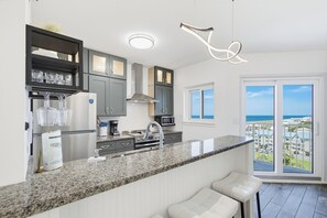 Eine moderne Küche mit Granit-Arbeitsplatten, Edelstahlgeräten und Meerblick vom Balkon aus.