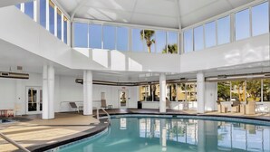Une grande piscine intérieure à l’eau d’un bleu limpide, entourée de murs blancs et de grandes fenêtres.