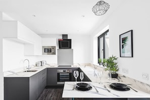 A modern kitchen with a central island, built-in appliances, and a dining area set for four. - Horizon View by MyCityHaven (Redland)