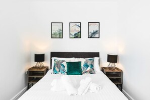 A neatly made bed with white linens and two pillows, flanked by two bedside tables with lamps, and three framed artworks on the wall above. - Horizon View by MyCityHaven (Redland)