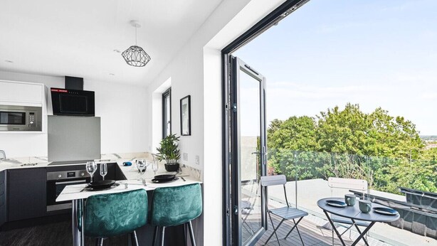 Een moderne keuken met een eethoek, een grote schuifpui naar een terras en uitzicht op groen.