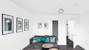 Een moderne woonkamer met een grijze bank, twee ronde houten tafels en kunstwerken in lijsten aan de muren.