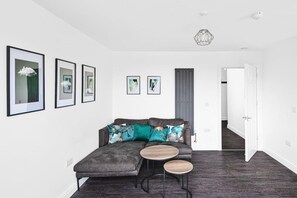 A modern living room with a grey sofa, two round wooden tables, and framed artwork on the walls. - Horizon View by MyCityHaven (Redland)