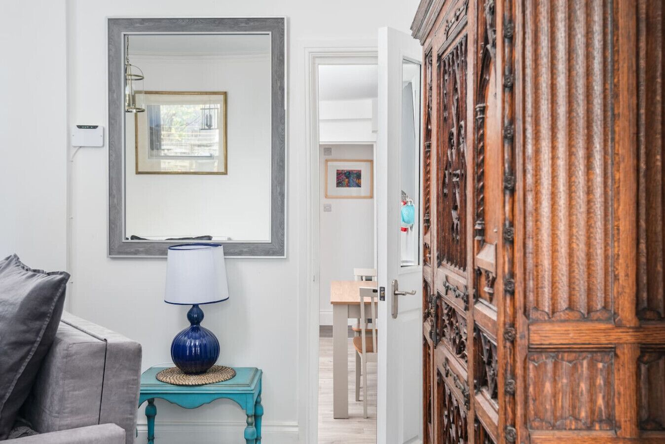 Een kamer met een bank, een lamp, een spiegel en een houten kast.