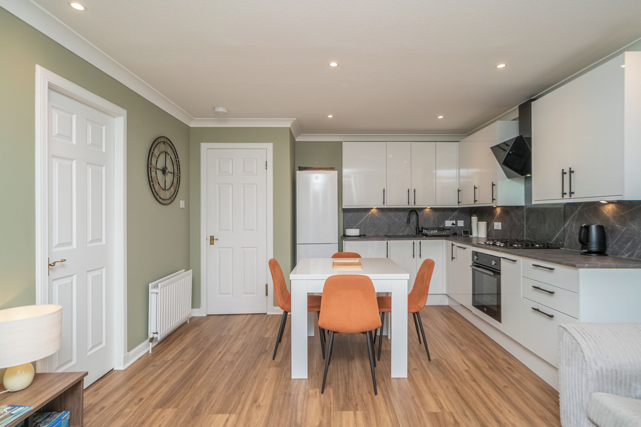 A modern kitchen with white cabinets, a dining table with orange chairs, and a built-in oven.