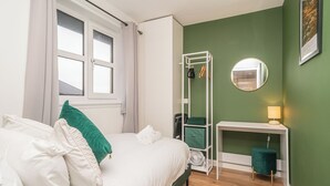 Ein Schlafzimmer mit einem Bett, einem Nachttisch, einem Spiegel, einer grünen Wand und einem Fenster.