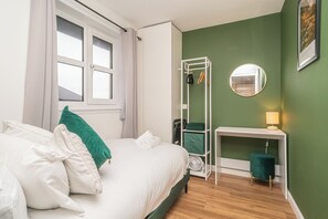 Ein Schlafzimmer mit einem Bett, einem Nachttisch, einem Spiegel, einer grünen Wand und einem Fenster.