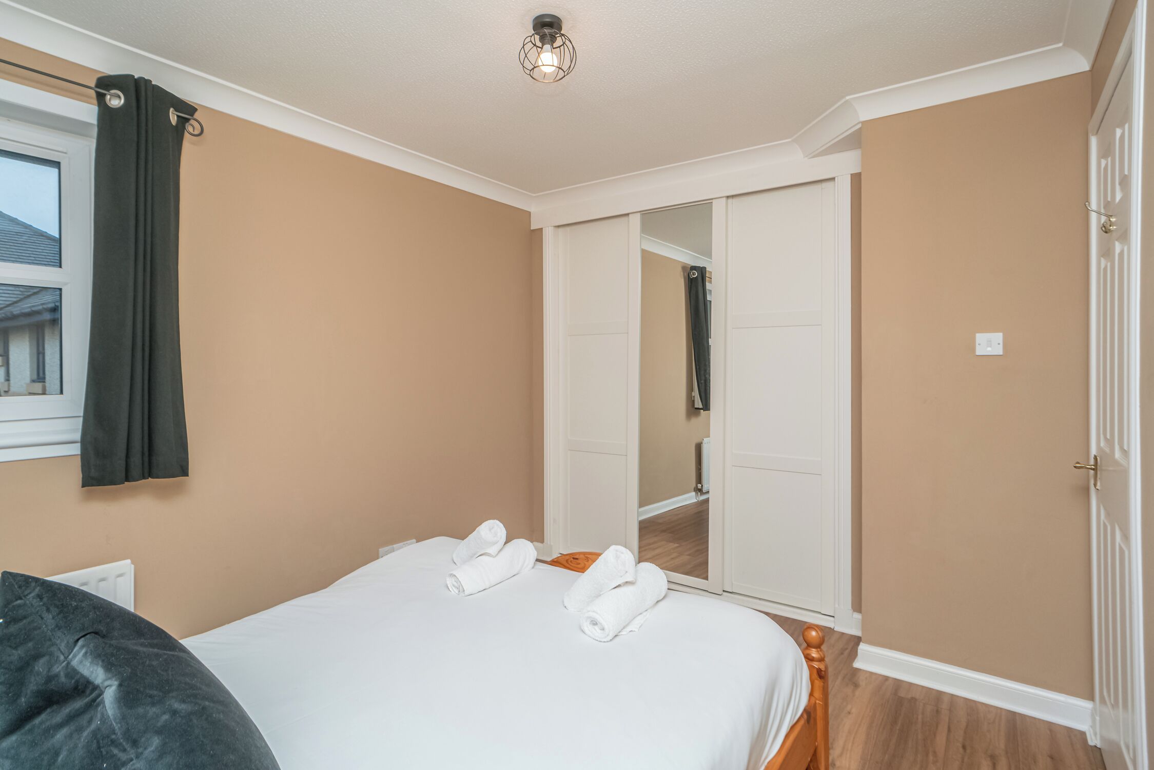 A hotel room with a bed, a mirror, a wardrobe, and a door.