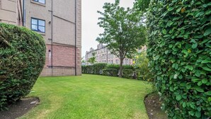 Ein gepflegter Rasenhof mit Hecke, Baum und einem Gebäude mit mehreren Fenstern.