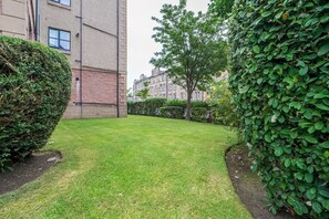Ein gepflegter Rasenhof mit Hecke, Baum und einem Gebäude mit mehreren Fenstern.