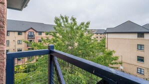 Ein Wohngebäude mit mehreren Balkonen, einem Metallzaun und einem Baum im Vordergrund.