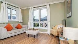 Ein Wohnzimmer mit Sofa, Hocker, Sessel und einem Tisch mit Lampe und Fernbedienung.