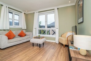 Ein Wohnzimmer mit Sofa, Hocker, Sessel und einem Tisch mit Lampe und Fernbedienung.