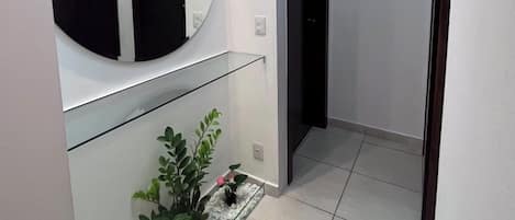A hallway with a glass partition, a round mirror, and a potted plant.