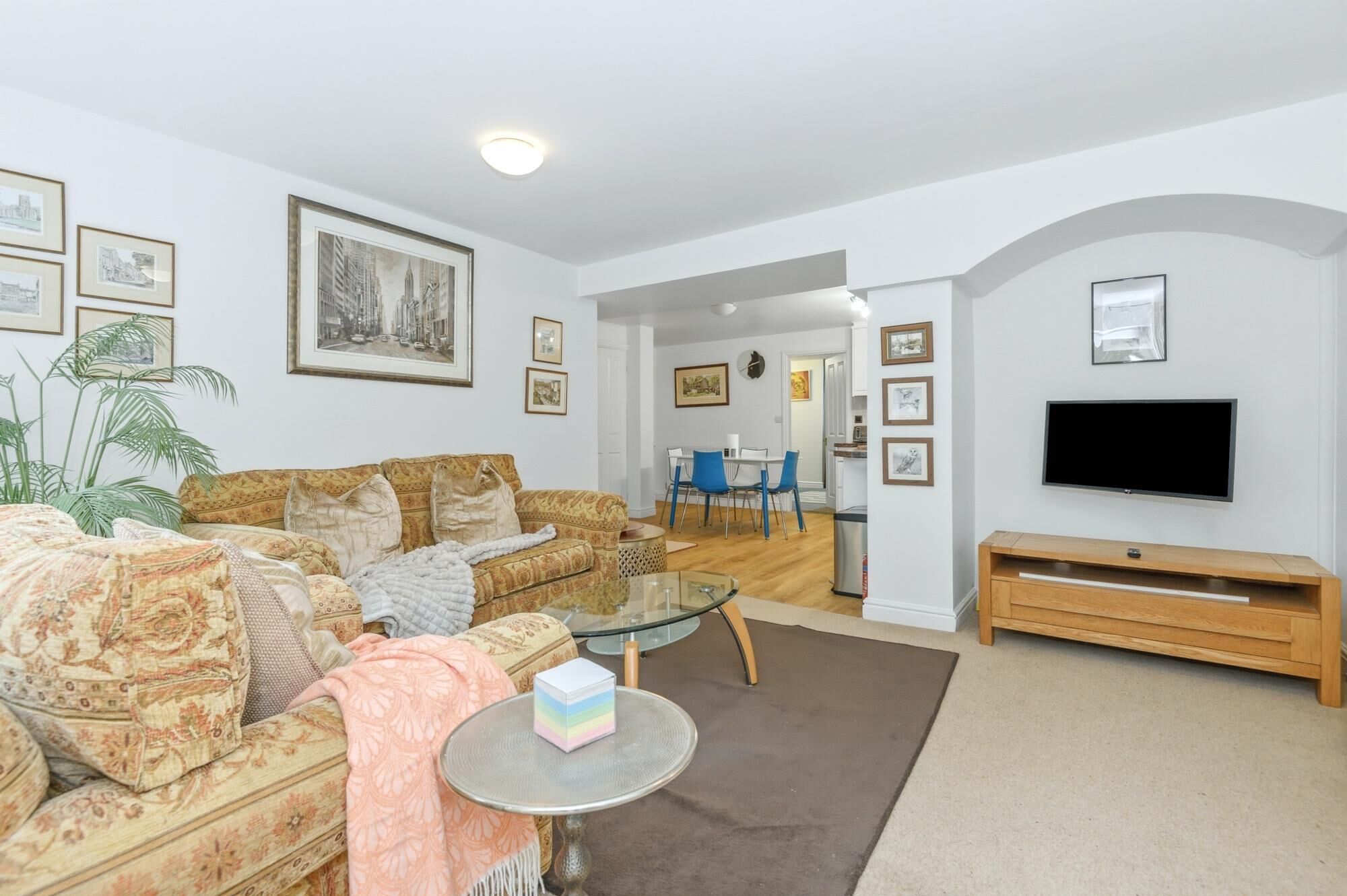 A living room with a sofa, a glass coffee table, a TV, and framed pictures on the walls.