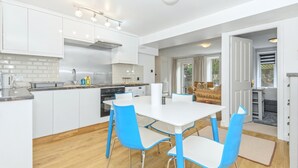 Une cuisine moderne avec des meubles blancs, un îlot central et un coin repas avec des chaises bleues.
