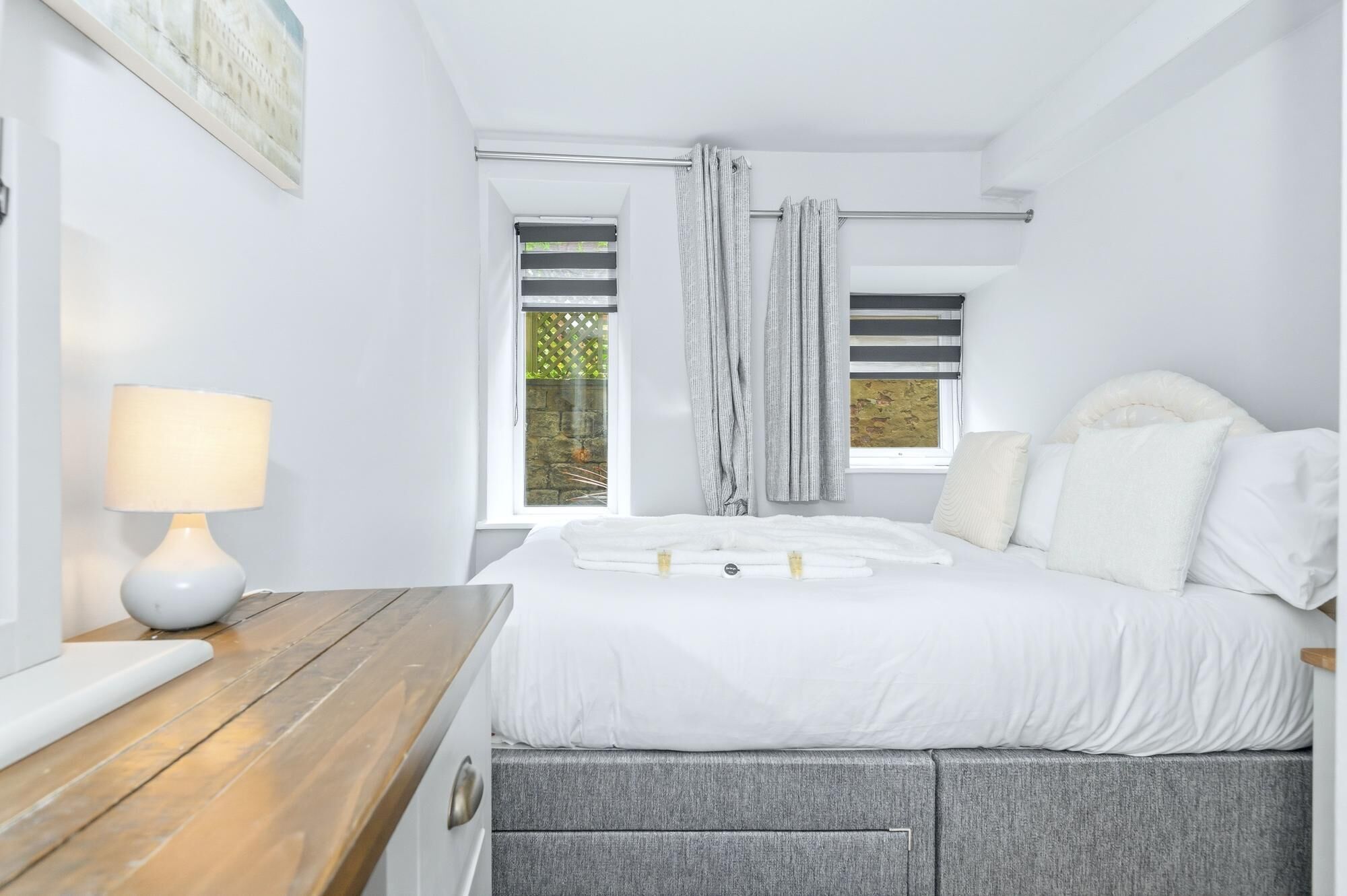 A bedroom with a bed, a bedside table, a lamp, and a window with curtains.