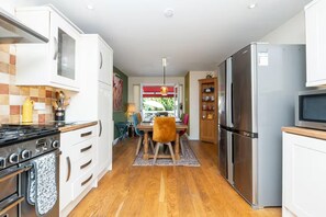 A modern kitchen with a stove, oven, refrigerator, and microwave. There is a dining area with a table and chairs. - Large family home on the outskirts of Bath - Pass the Keys (Bath)