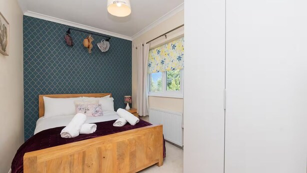 Quarto com cama de madeira, janela com cortinas florais e parede com padrão geométrico.