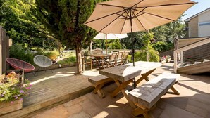 Um pátio com mesas e cadeiras de madeira, um grande guarda-sol e um deck de madeira.