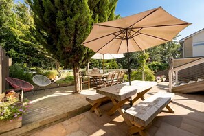 A patio with wooden tables and chairs, a large umbrella, and a wooden deck. - Large family home on the outskirts of Bath - Pass the Keys (Bath)
