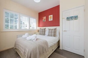 Una camera d'albergo con un letto, un termosifone, una finestra con tende, una porta e decorazioni alle pareti.