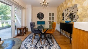 Uma sala de jantar com mesa de vidro, duas cadeiras, um candelabro e um relógio de parede.