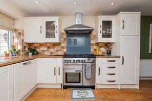 Una cucina con mobili bianchi, piano cottura a gas, forno e schienale piastrellato.