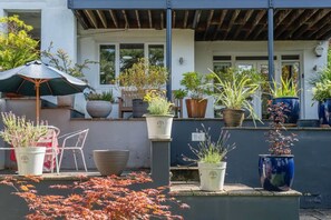Eine Terrasse mit Blumentöpfen, einem Tisch und Stühlen sowie einem Sonnenschirm.