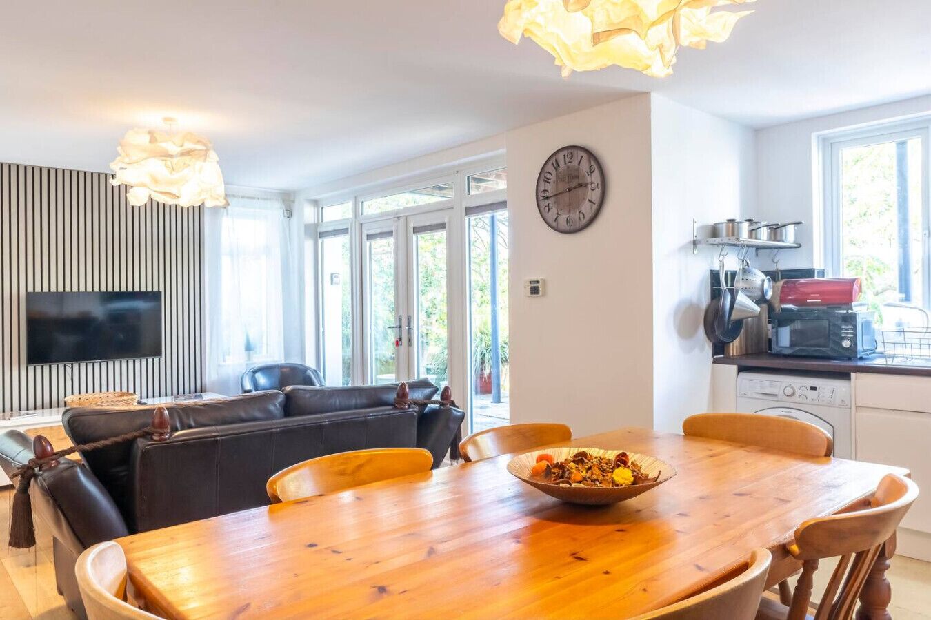 Een moderne woonruimte met een eethoek, een bank, een televisie en een keuken, met een klok aan de muur.