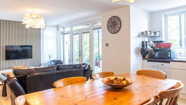 Ett modernt vardagsrum med en matplats, en soffa, en tv och ett köksområde med en klocka på väggen.