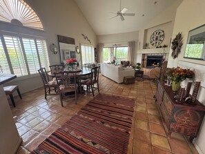 A spacious living area with a dining table, chairs, a sofa, a fireplace, and a large window with blinds. - Ventana Canyon Golf and Racquet Club 2-bedroom townhome (Tucson)