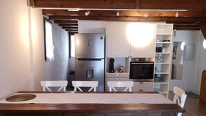 Een moderne keuken met witte kasten, een roestvrijstalen koelkast, een inbouwoven en een eethoek met een houten tafel en stoelen.