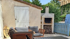Een terras buiten met houten meubilair, een barbecue en een witte deur.