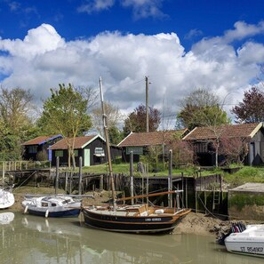 A rustic waterfront scene with boats docked, wooden houses, and a clear sky. - House with an enclosed, tree-lined garden in La Palmyre (Les Mathes)