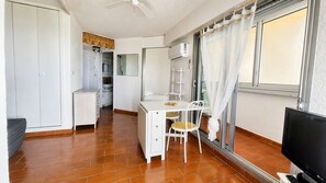 Ein kompaktes Zimmer mit Küchenzeile, einer Essecke mit Tisch und Stühlen, einem Fernseher und einem fenster mit Vorhängen.