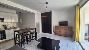 Eine moderne Küche mit Essbereich, einem Fernseher auf einer Holzkabine und einer Glastür, die auf einen Balkon führt.