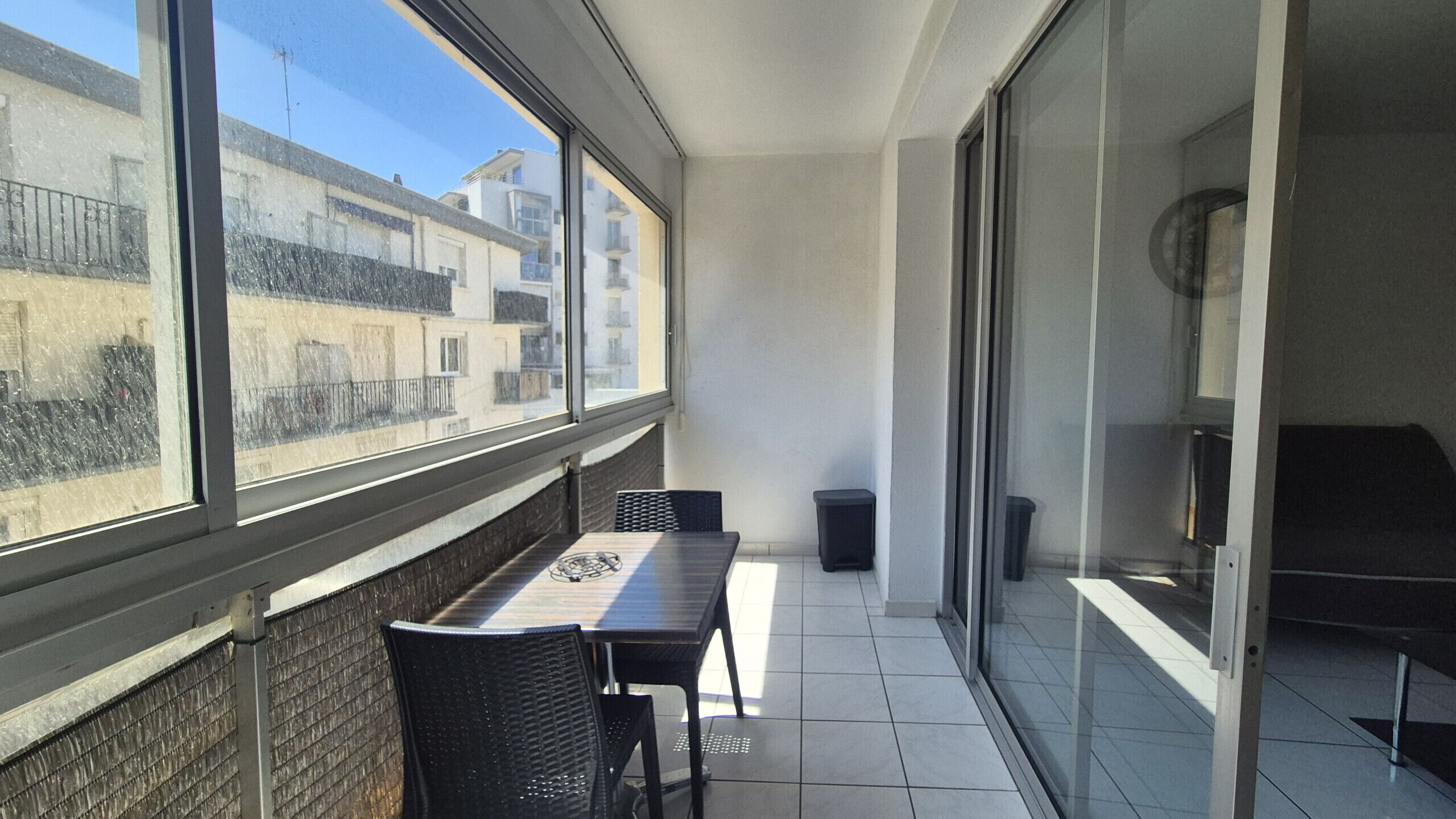 A balcony with a table and chairs, a trash bin, and a sliding glass door.