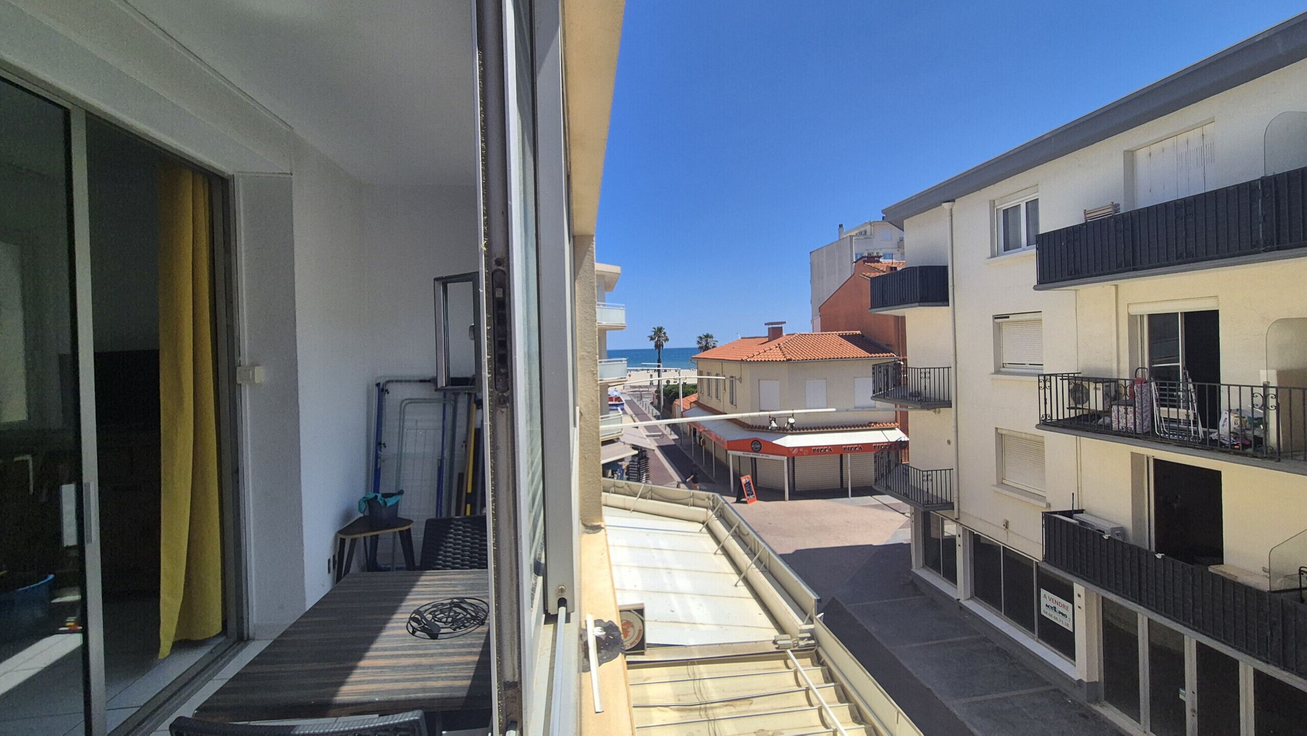 Una calle estrecha flanqueada por edificios, cielo azul despejado y una vista al mar en la distancia.