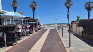 A street with a bike lane, palm trees, and a row of shops on the left. - Studio for 2 people with a loggia and partial sea view. (Canet-en-Roussillon)