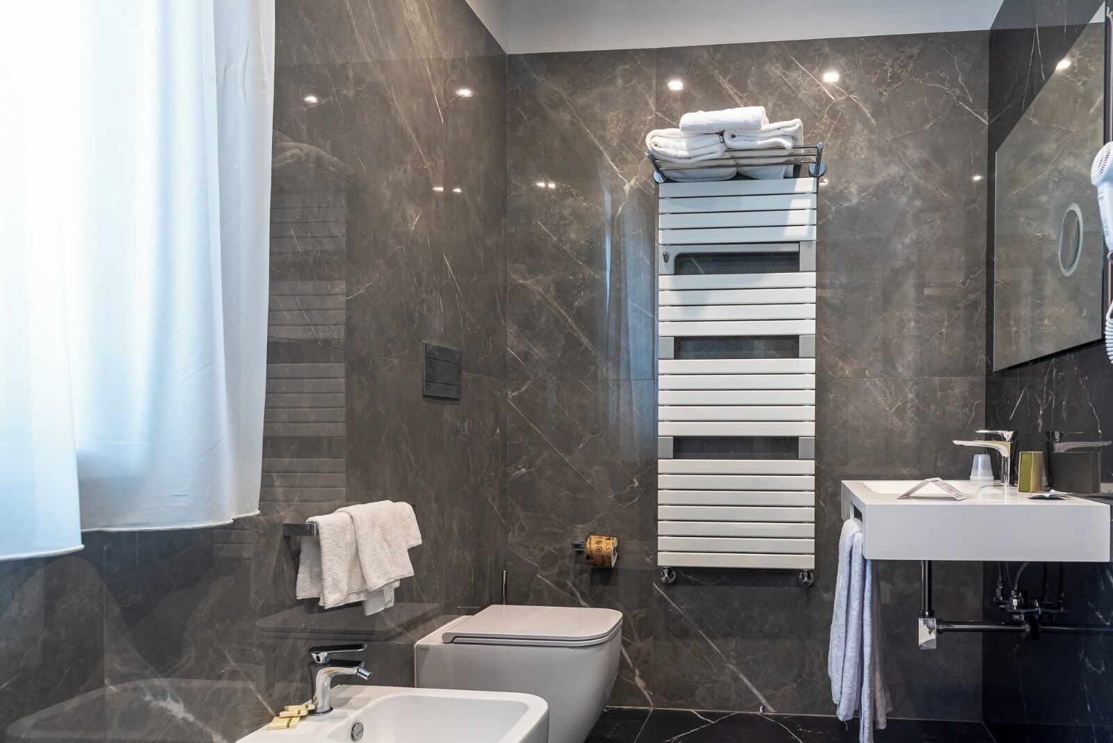 Un baño moderno con pared de mármol, un lavamanos blanco, un inodoro y un perchero con toallas dobladas.