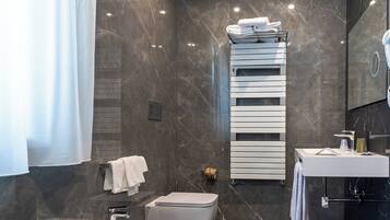 Un baño moderno con pared de mármol, un lavamanos blanco, un inodoro y un perchero con toallas dobladas.